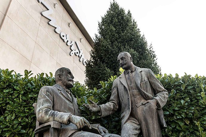 [Translate to Swiss German:] Zwei Männer im Anzug als Bronzestatuen vor einem Marzotto Gebäude.